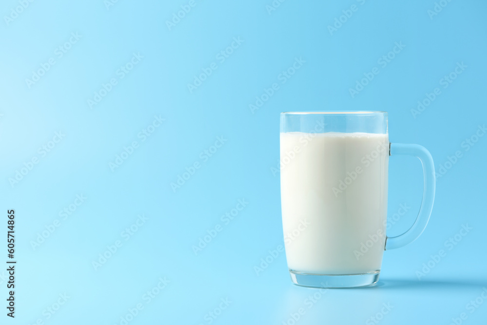 Glass mug of fresh milk on light blue background.