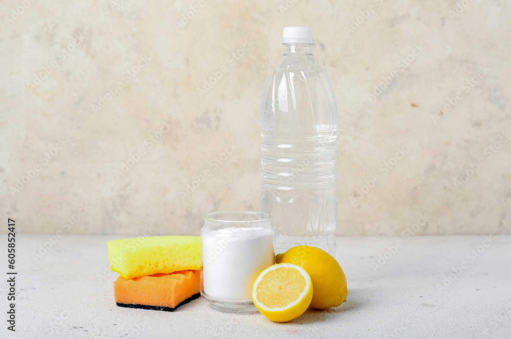 Glass of baking soda, vinegar, cleaning sponges and lemons on light table