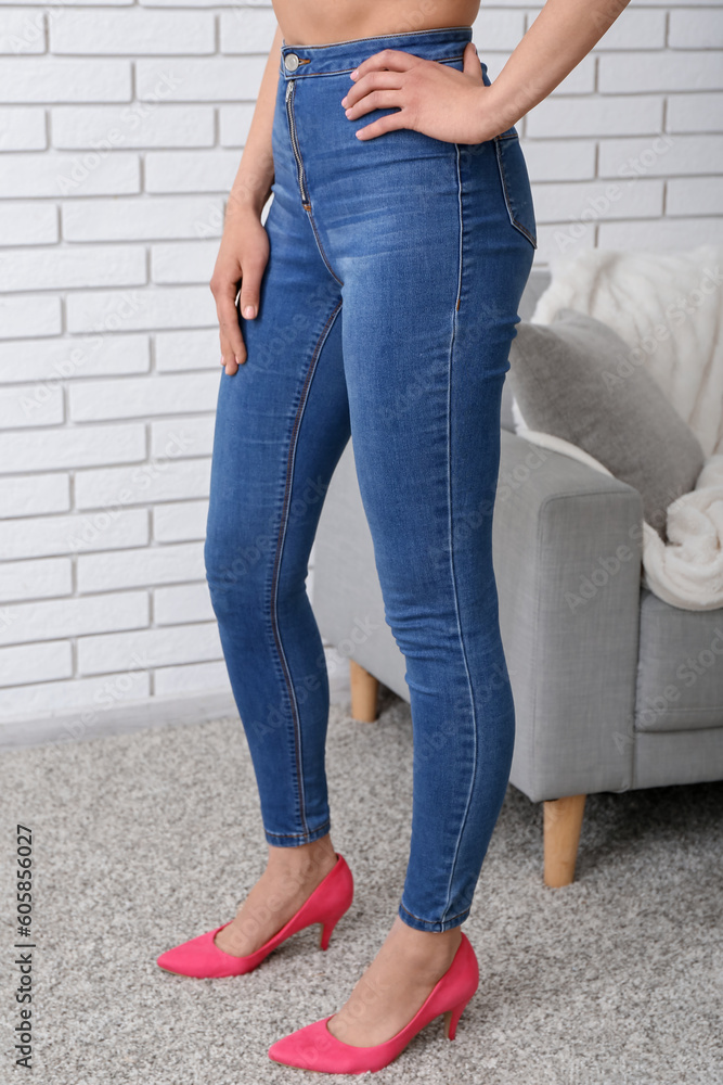 Young woman in stylish jeans and sofa near light brick wall in room