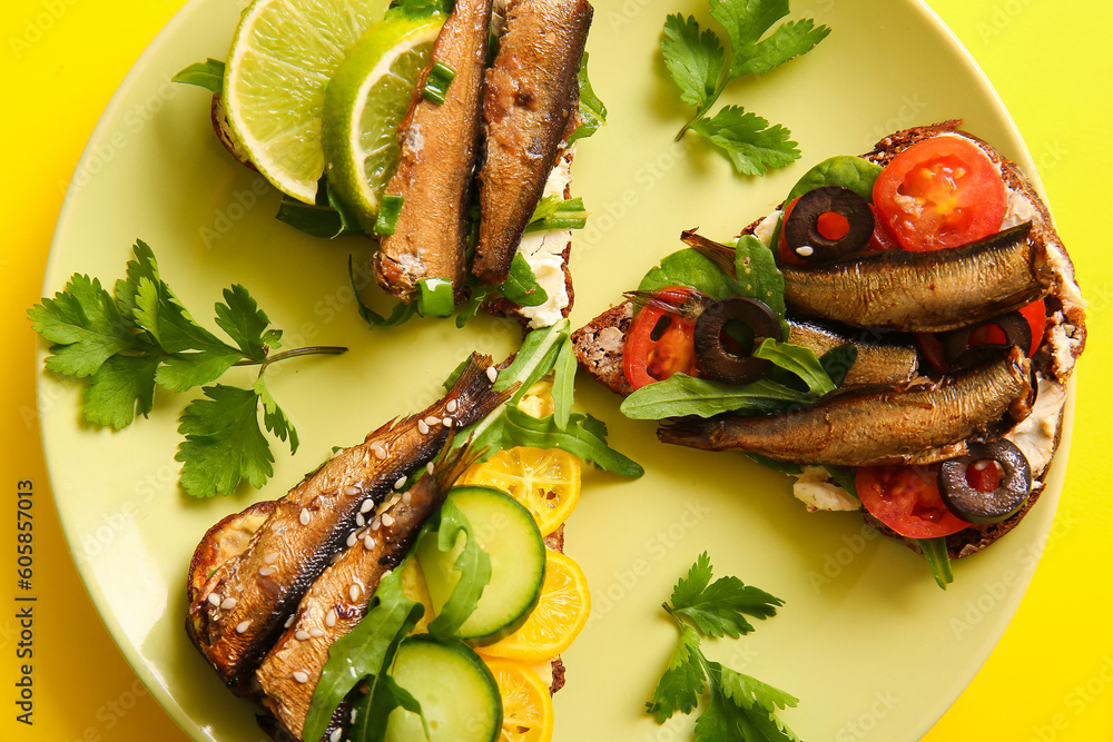 Plate of tasty sandwiches with canned smoked sprats on yellow background