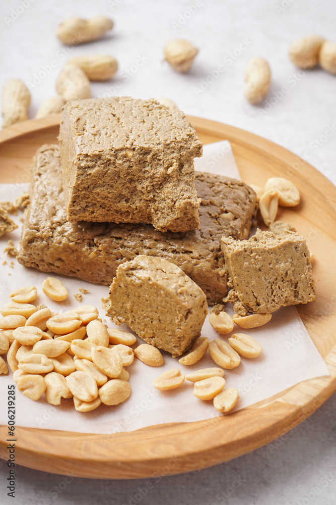 Wooden plate with pieces of tasty halva and peanuts on white background