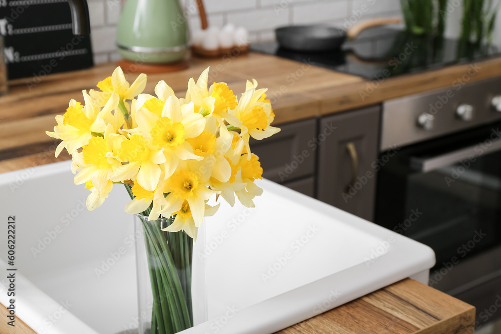 Vase with blooming narcissus flowers in sink, closeup