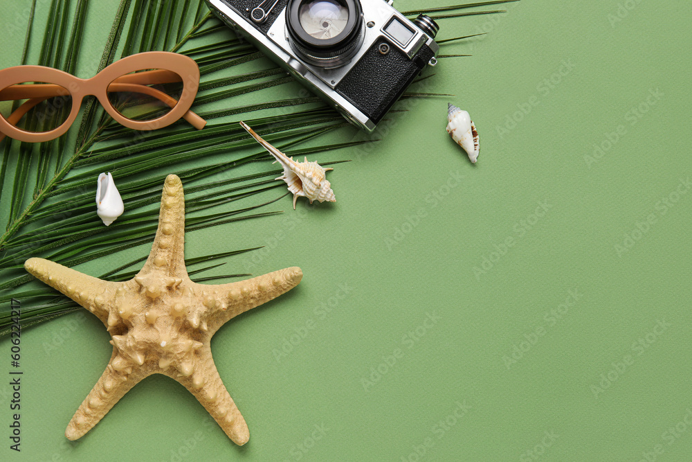 Composition with palm leaf, sunglasses, photo camera and seashells on green background