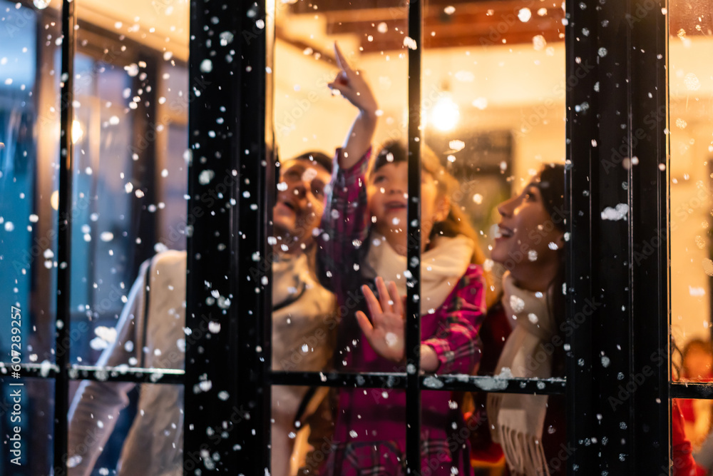 Adorable child looking at the window and first snow flakes with family. 