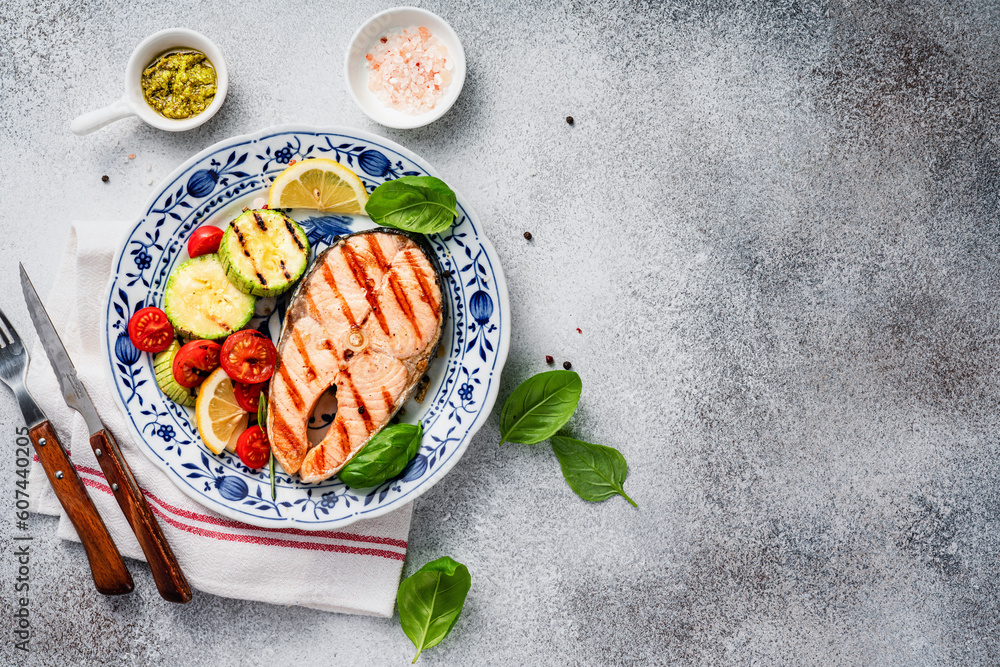 Grilled salmon steaks with spices, lemons and grilled zucchini on plate. Top view of fried fish. Ket