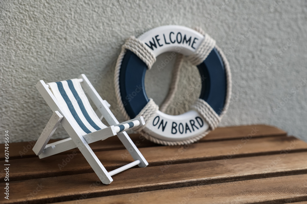 Toy sun lounger and ring buoy on table near light wall