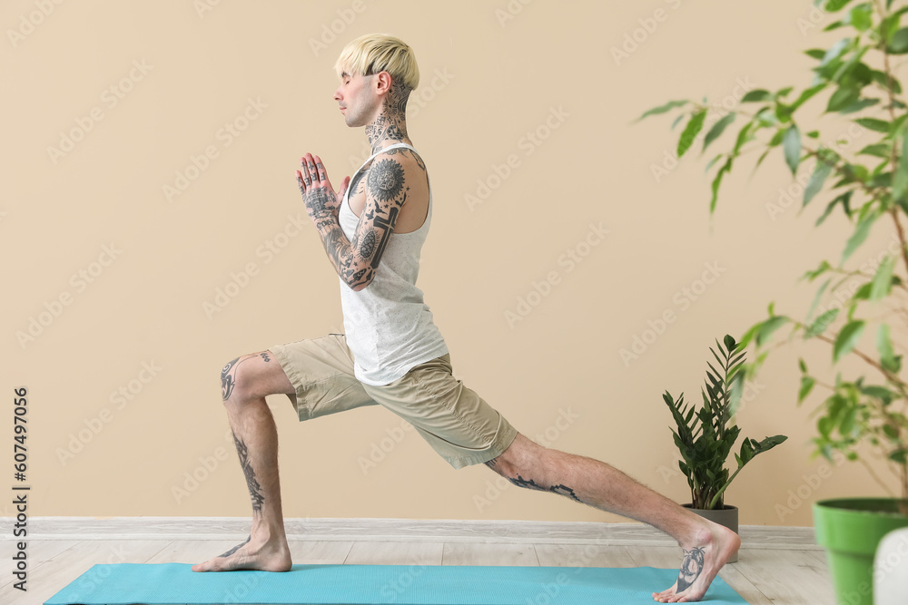 Tattooed young man doing yoga near beige wall