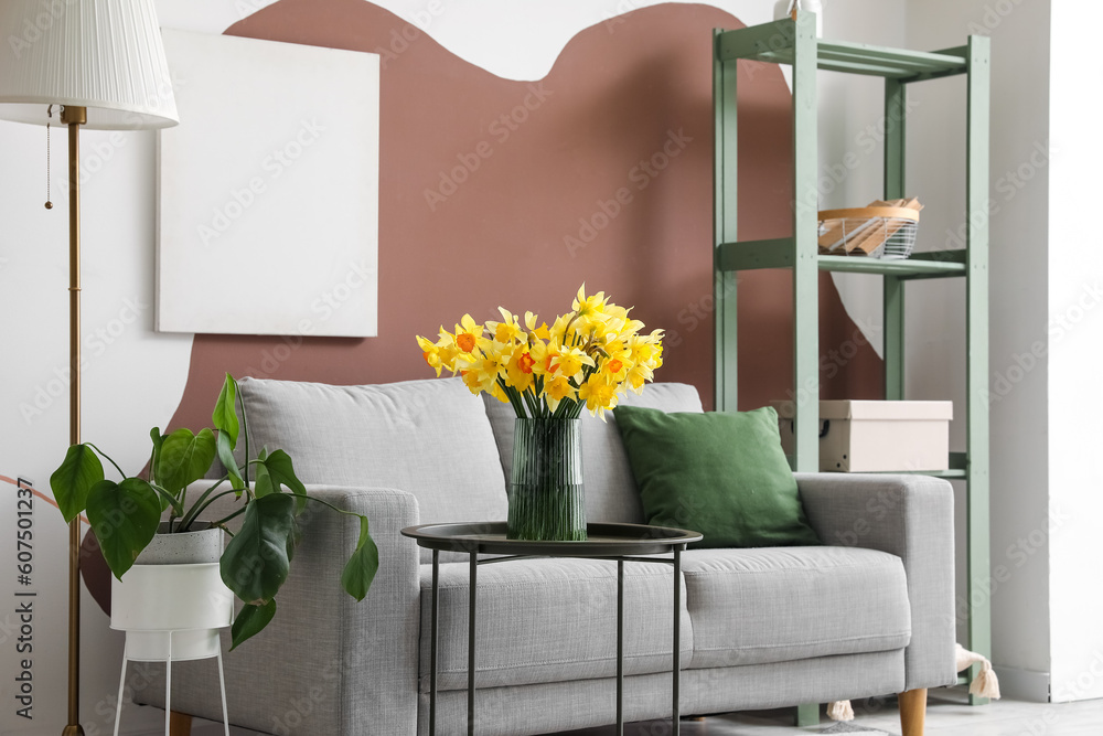 Interior of stylish living room with cozy grey sofa and blooming narcissus flowers on coffee table