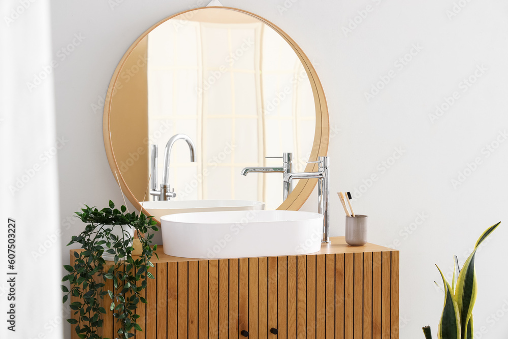 Wooden cabinet with sink, mirror and houseplant in interior of bathroom