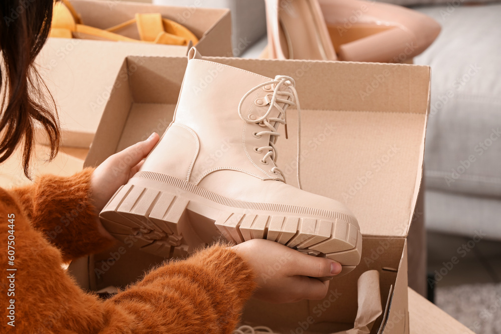 Woman taking beige boots out of box in room