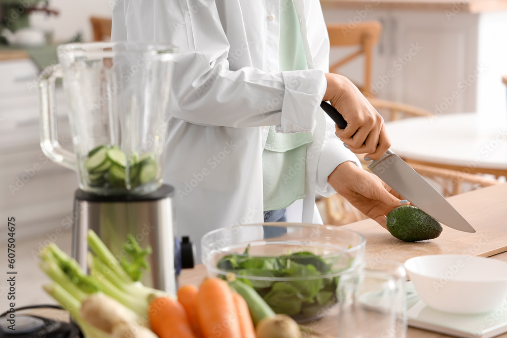 Young woman cutting avocado for vegetable juice in kitchen, closeup