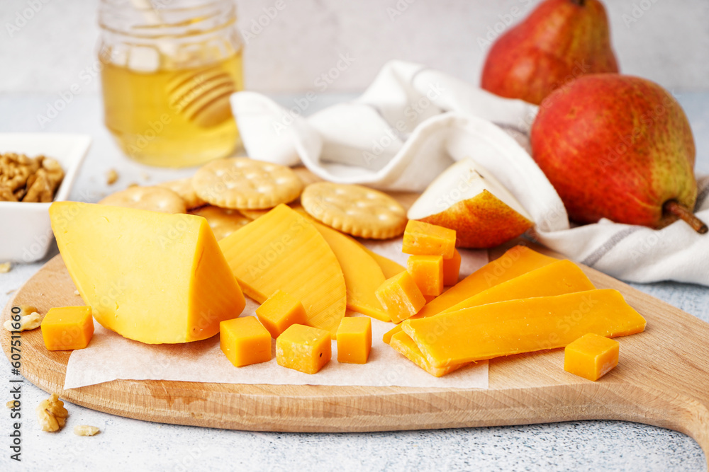 Board with tasty cheddar cheese, crackers and pear on light background, closeup