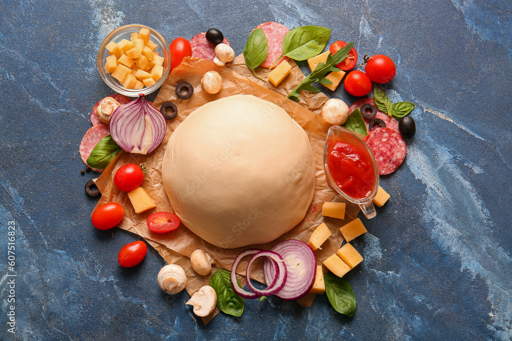 Baking paper with raw dough and ingredients for preparing pizza on blue background