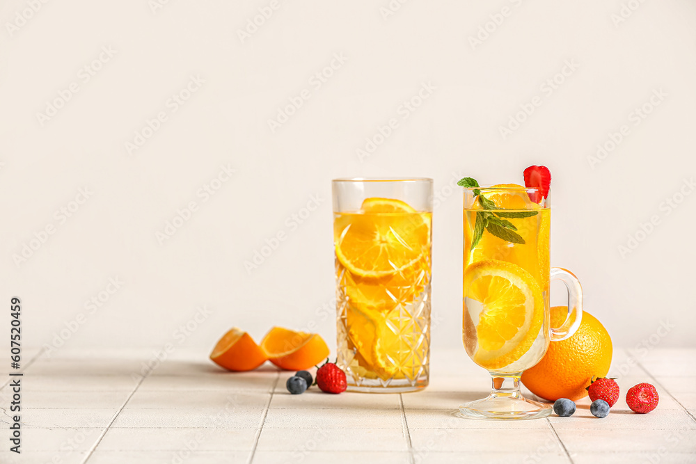 Glasses of infused water with orange slices on white tile background