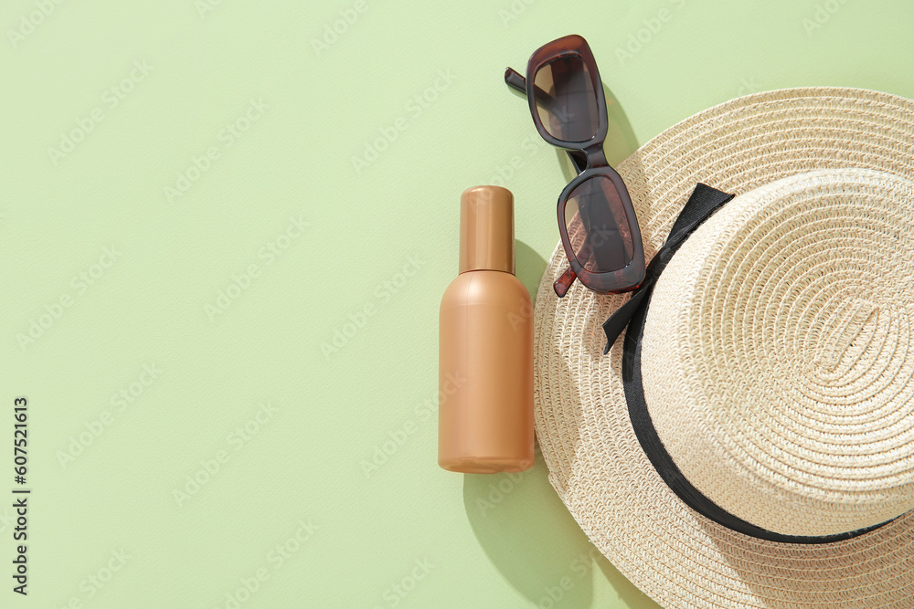 Bottle of sunscreen cream with sunglasses and summer hat on green background