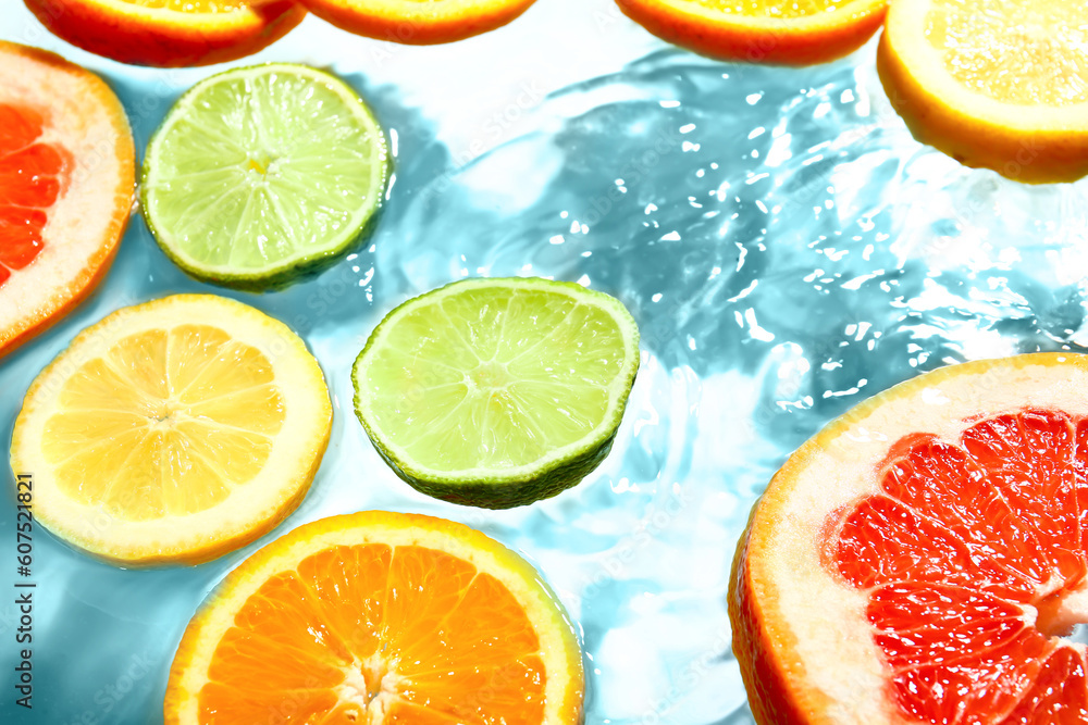 Different citrus fruit slices in water on blue background