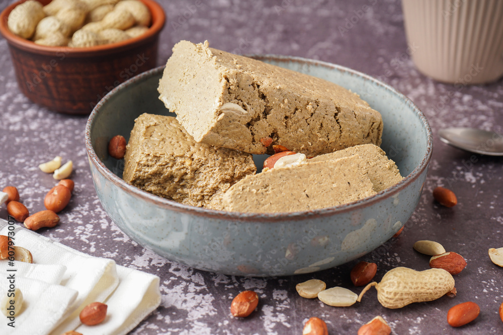 Bowl with pieces of tasty halva and peanuts on grey background