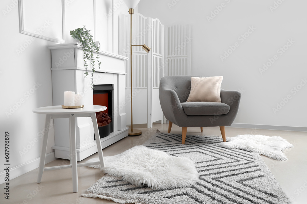 Cozy grey armchair with cushion, fireplace and folding screen in interior of living room