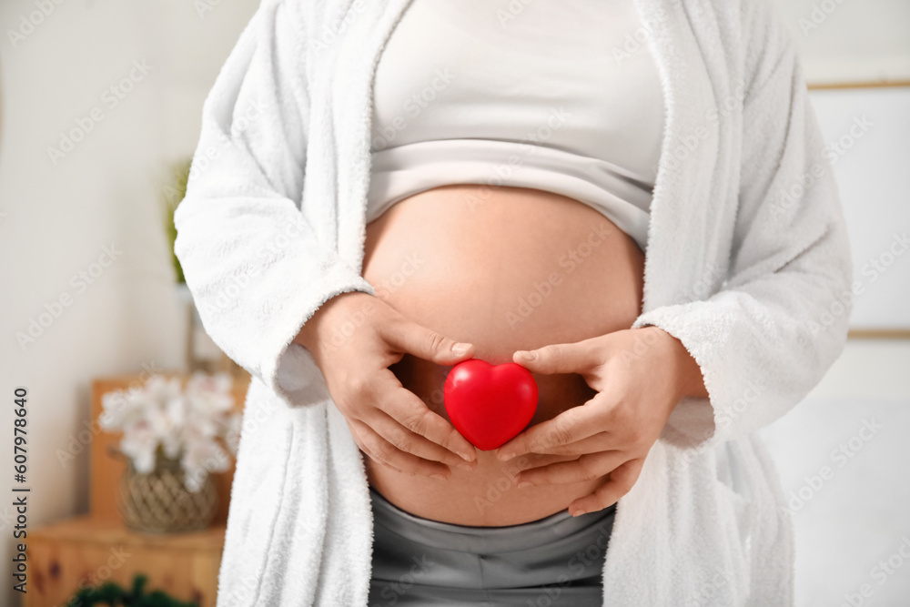 Young pregnant woman with heart in bedroom, closeup