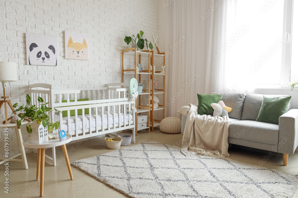 Interior of light bedroom with baby crib, sofa and shelving unit