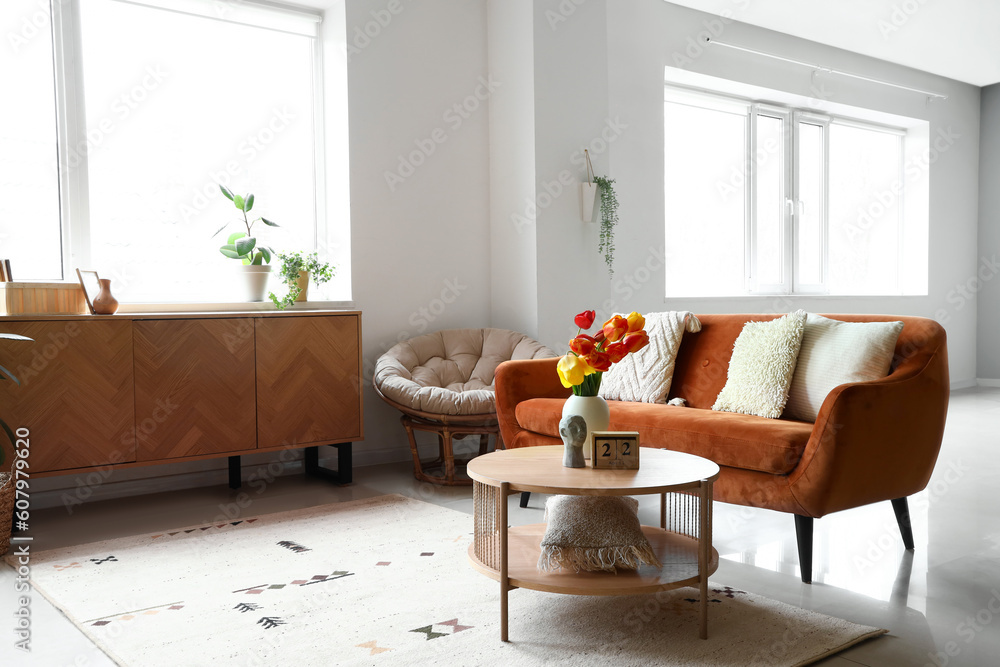 Interior of light living room with cozy sofa and tulip flowers on coffee table