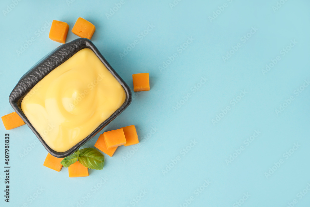 Bowl with tasty cheddar cheese sauce on blue background