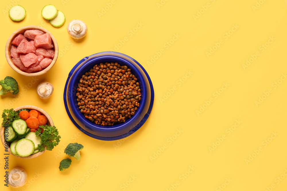 Bowls with dry pet food, raw meat and natural products on yellow background