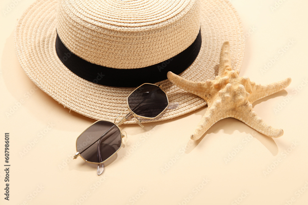 Stylish sunglasses with hat and starfish on beige background