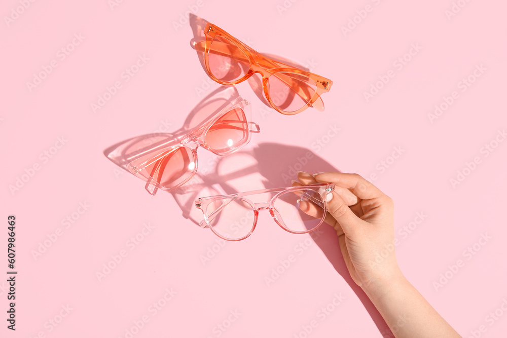 Female hand holding stylish sunglasses on pink background