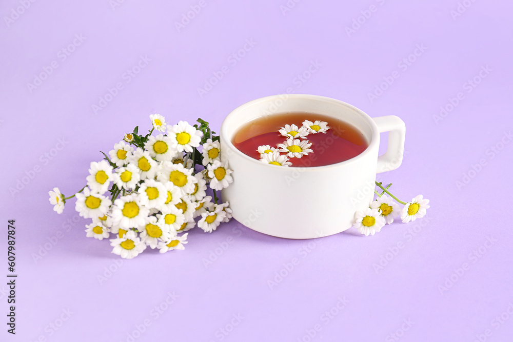 Cup of natural chamomile tea and flowers on lilac background