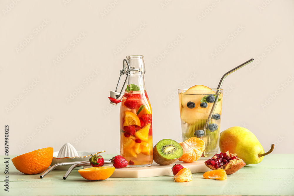 Glass and bottle of infused water with different sliced fruits on green wooden table