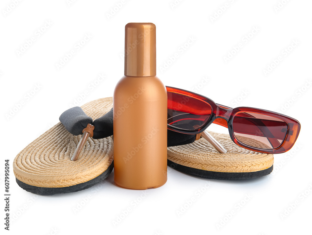 Bottle of sunscreen cream with sunglasses and wicker flip flops isolated on white background