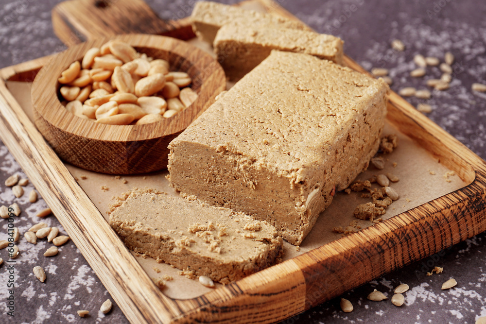 Board with pieces of tasty halva, peanuts and sunflower seeds on grey background