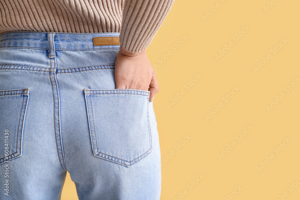 Young woman in stylish jeans on yellow background, back view