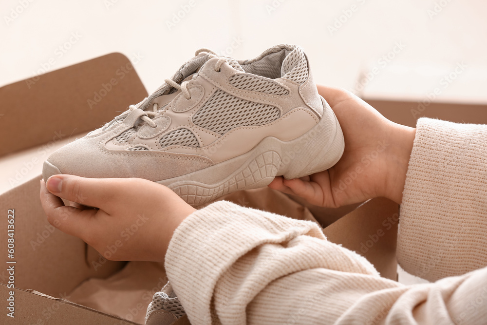 Woman taking grey sneakers out of box in room