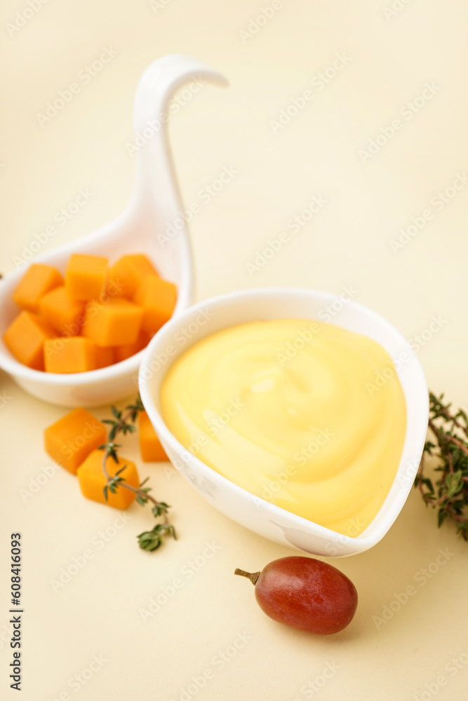 Bowl with tasty cheddar cheese sauce, thyme and grape on beige background, closeup