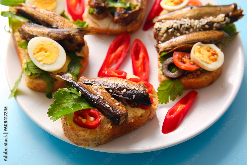 Plate of tasty sandwiches with canned smoked sprats on blue background