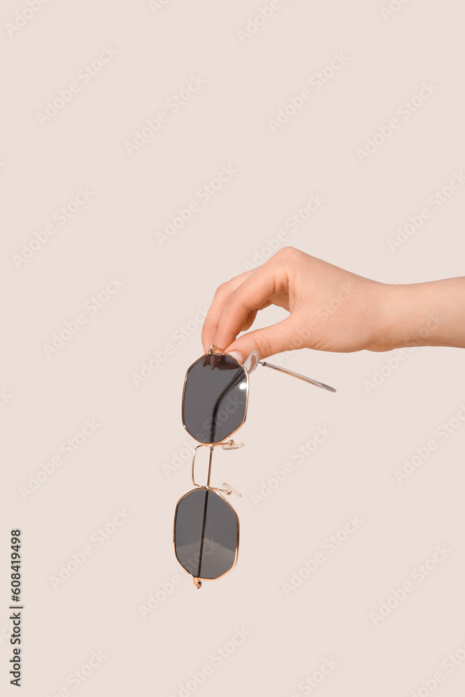 Female hand holding stylish sunglasses on grey background