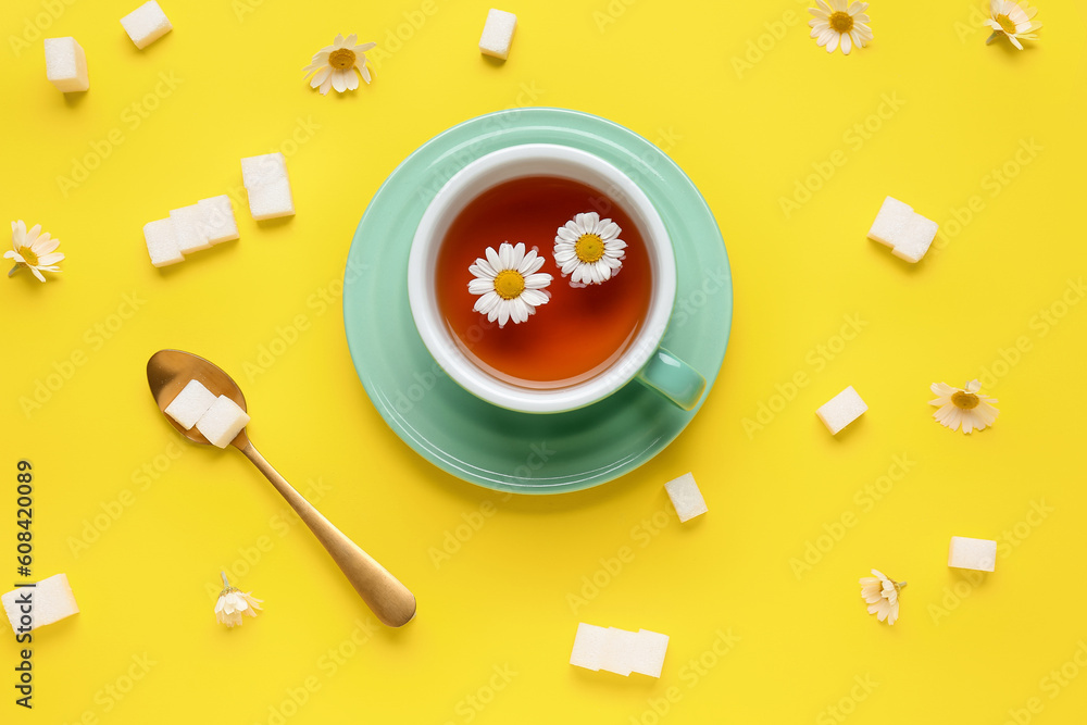 Cup of natural chamomile tea, sugar cubes and flowers on yellow background