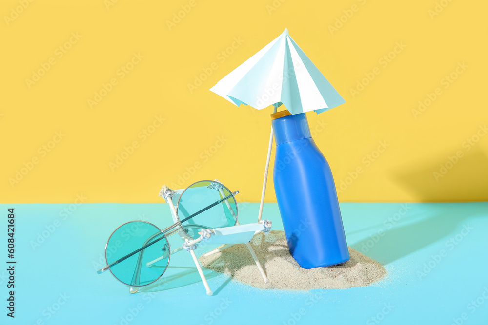 Creative composition with miniature deckchair, sunglasses and bottle of sunscreen cream on blue tabl