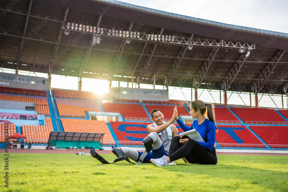 Asian para-athlete with prosthetic blades and trainer sit in stadium. 