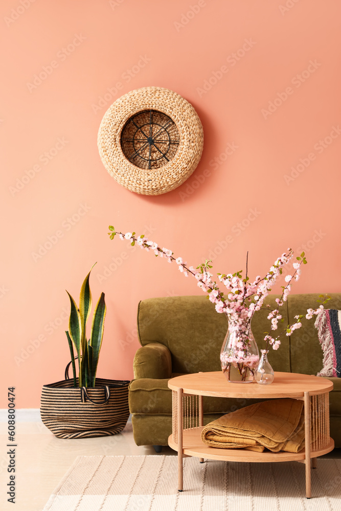 Interior of cozy living room with green sofa and blooming sakura branches on coffee table