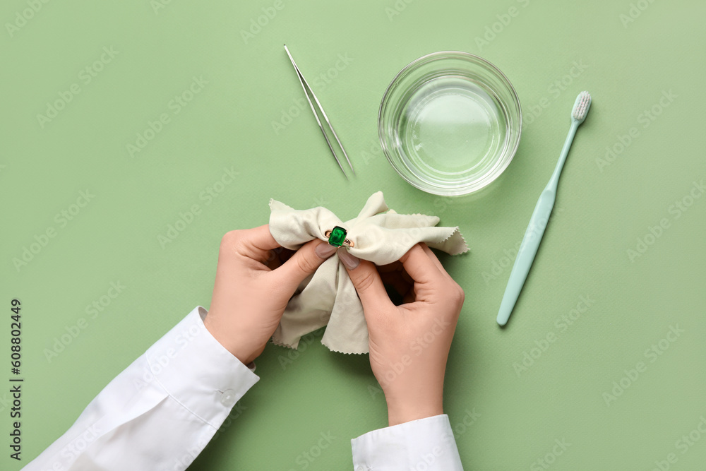 Woman polishing beautiful ring with napkin on green background, closeup