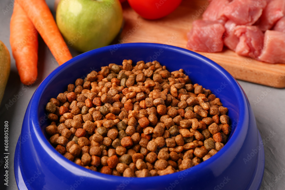 Bowl with dry pet food, raw meat and natural products on color wooden background, closeup