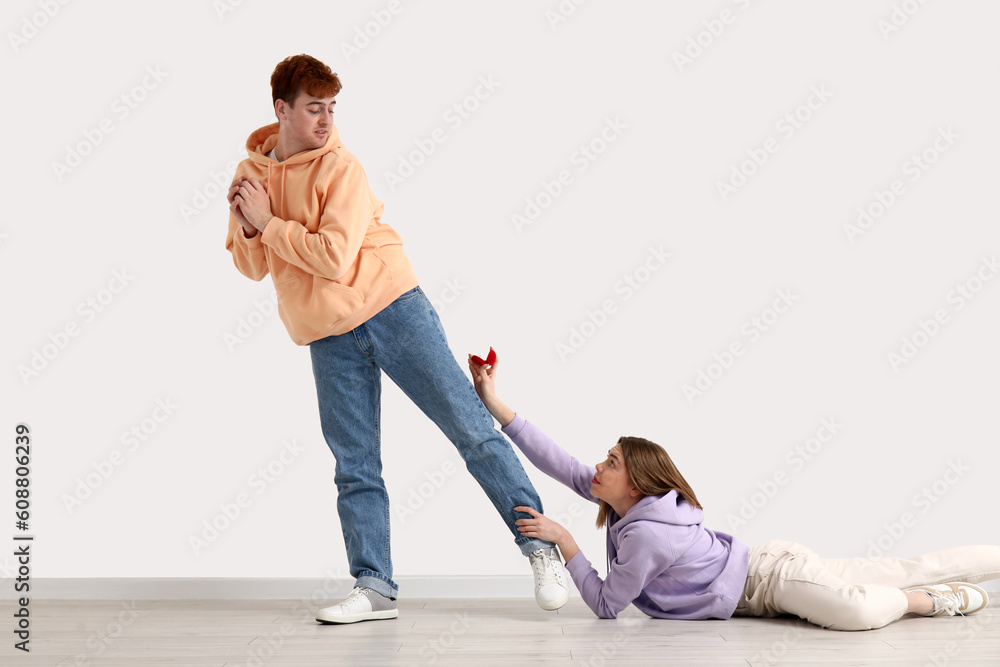 Young woman begging her boyfriend to marry her near light wall