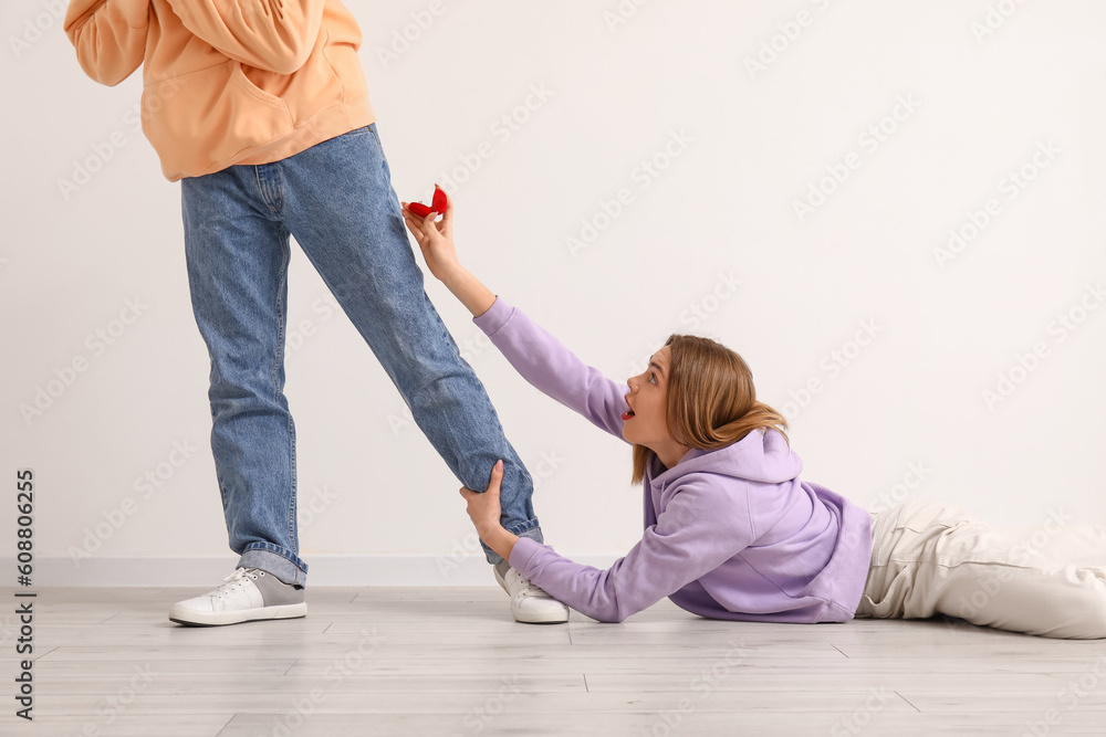 Young woman begging her boyfriend to marry her near light wall