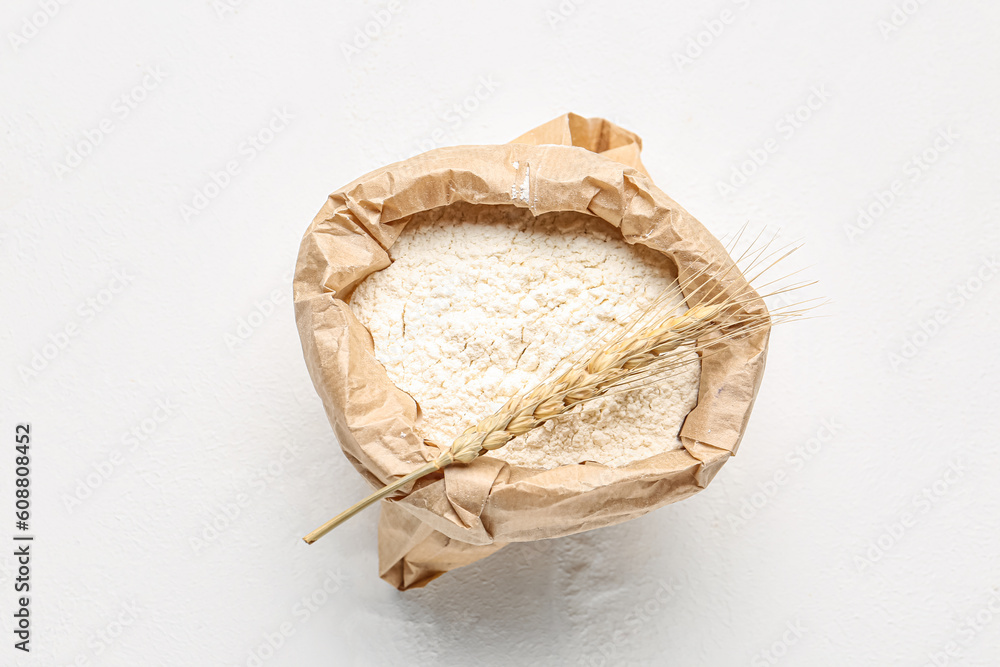 Paper bag with flour and wheat ear on white background