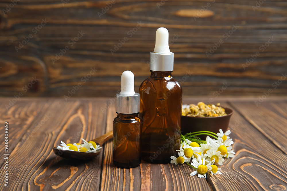 Bottles of essential oil, fresh and dried chamomile flowers on wooden background