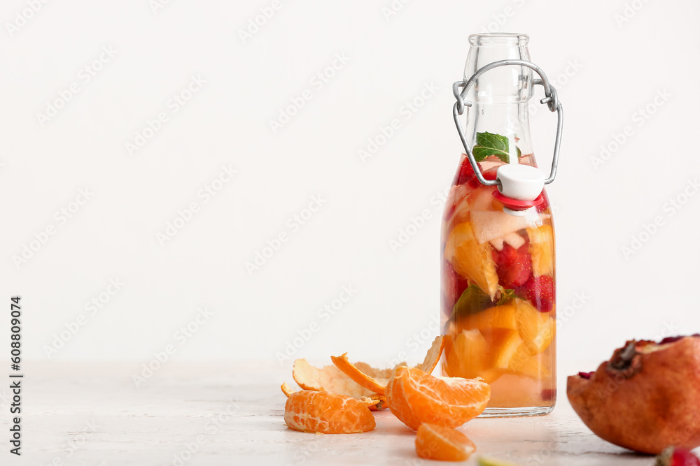 Bottle of infused water with different sliced fruits on white table