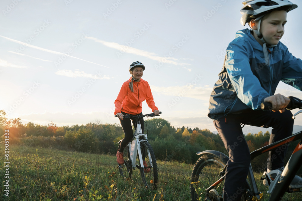 Mother and son ride bike outdoors. Happy cute boy in helmet to riding a bike in park on green meadow